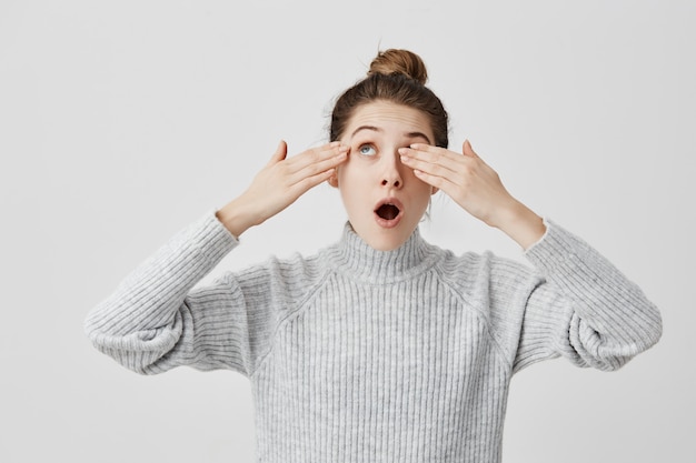 Aantrekkelijk meisje die hipster haar ogen verbergen van zon die het met handen behandelen. Jonge vrouw die omhoog met geopende mond kijkt wordt verblind door zonneschijn. Lichaamstaal