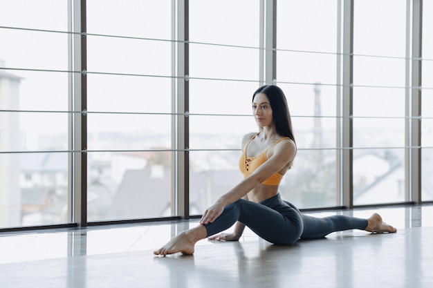 Aantrekkelijk meisje doet fitness oefeningen met yoga op de vloer tegen het oppervlak van panoramische ramen