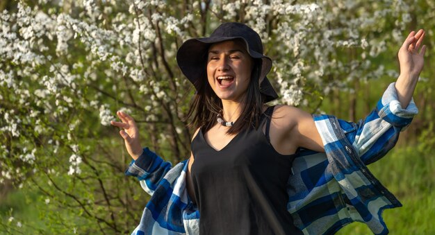Aantrekkelijk meisje in een hoed tussen de bloeiende bomen in het voorjaar, in een casual stijl.