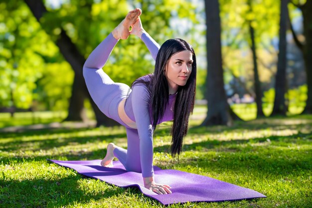 Aantrekkelijk meisje met lang zwart haar gekleed in paars doet yoga pose Een been duif