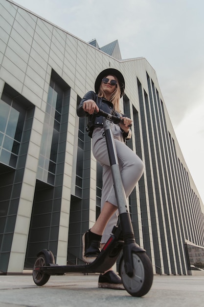 Aantrekkelijk modieus meisje in zonnebril en hoed poseert voor fotograaf met haar nieuwe scooter.