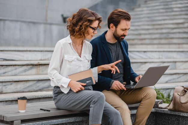 Aantrekkelijk paar man en vrouw praten zittend op trappen in het centrum van de stad, samenwerken op laptop
