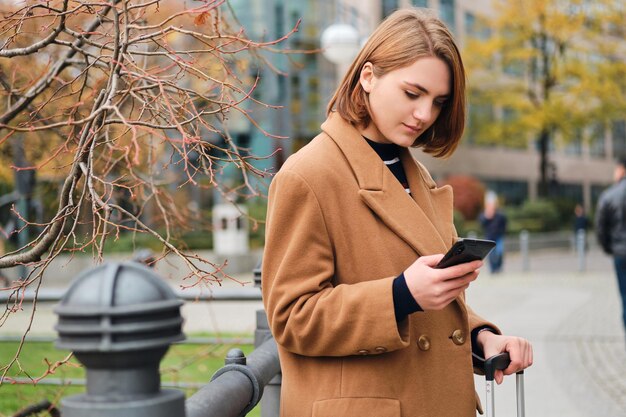 Aantrekkelijk stijlvol meisje dat zorgvuldig mobiele telefoon gebruikt op straat in de stad