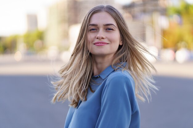 Aantrekkelijk vrolijk blondemeisje met vliegend lang haar glimlachend lachend in de stad