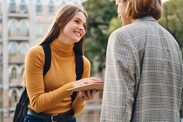 Aantrekkelijk vrolijk casual studentenmeisje dat graag met een vriend praat tijdens studiepauze buiten