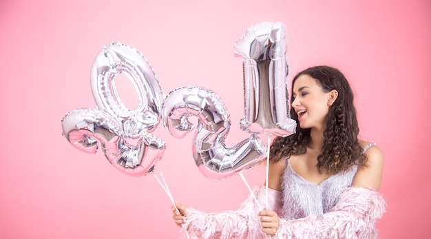 Aantrekkelijk vrolijk meisje op een roze achtergrond met zilveren ballonnen voor het nieuwe jaar in haar handen