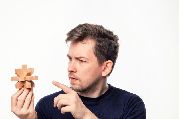 Aantrekkelijke 25-jarige zakenman op zoek verward houten puzzel.