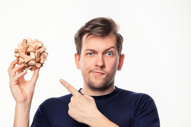 Aantrekkelijke 25-jarige zakenman op zoek verward met houten puzzel.