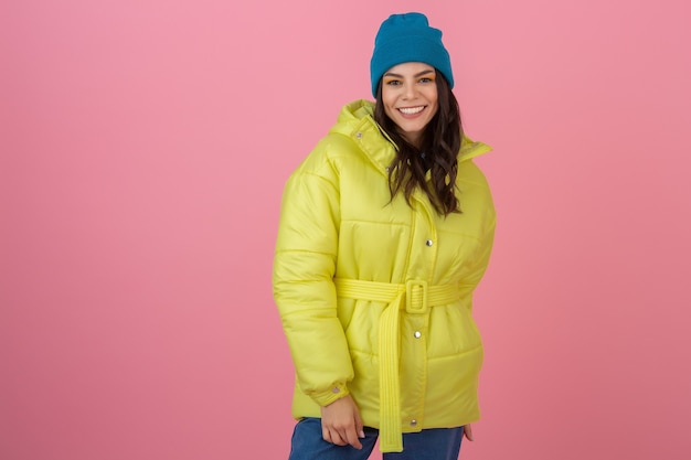 Aantrekkelijke actieve vrouw die zich voordeed op roze muur in kleurrijke winter donsjack van felle gele kleur, glimlachend plezier, warme vacht modetrend, gek geschokt verrast gezicht expressie