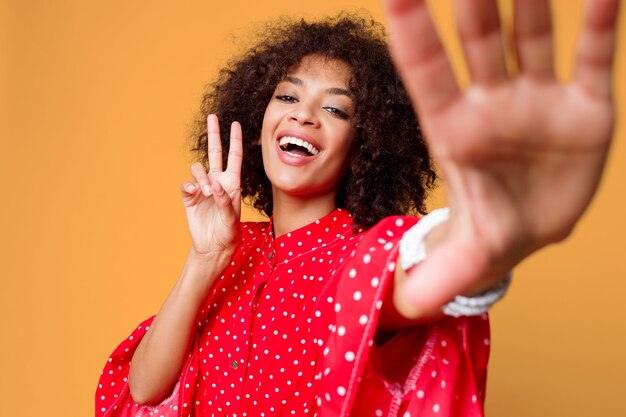 Aantrekkelijke Afrikaanse vrouw die met golvende haren zelfportret over gele muur maakt.