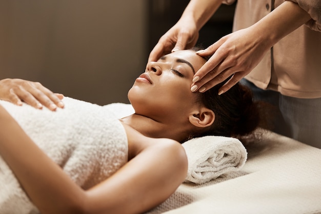 Aantrekkelijke afrikaanse vrouw genieten van gezichtsmassage in spa salon.