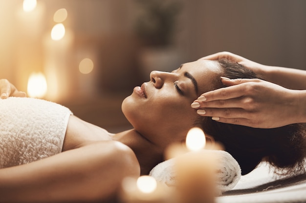 Aantrekkelijke Afrikaanse vrouw genieten van gezichtsmassage in spa salon.