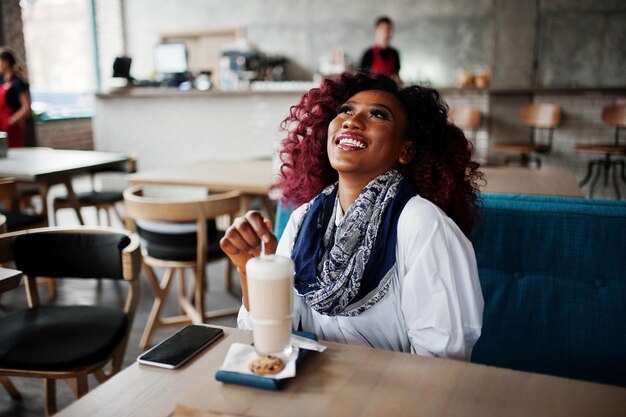 Aantrekkelijke Afro-Amerikaanse krullend meisje zit in café met latte