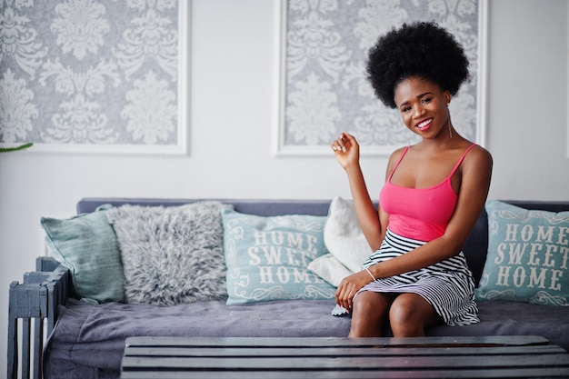 Aantrekkelijke afro-amerikaanse vrouw met afro-haar op rok roze top geposeerd in witte kamer Modieus sexy zwart model