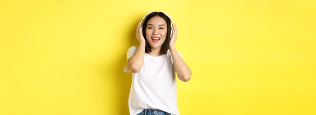 Aantrekkelijke aziatische vrouw die geniet van het luisteren naar muziek in draadloze hoofdtelefoons die tevreden glimlacht en a zingt