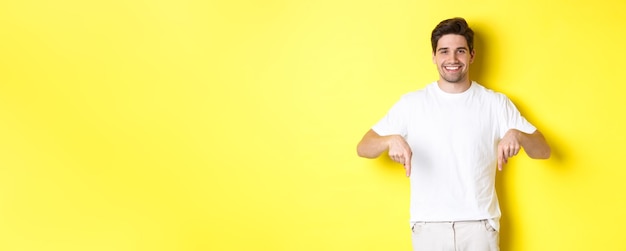 Gratis foto aantrekkelijke bebaarde man die met zijn vingers naar beneden wijst en een spandoek laat zien die over een gele achtergrond staat
