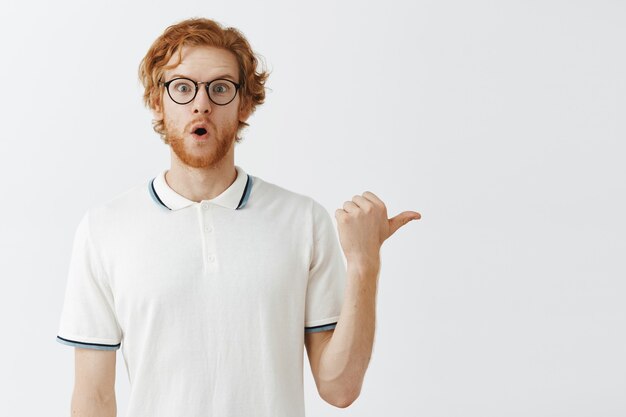 Aantrekkelijke bebaarde roodharige man poseren tegen de witte muur met bril