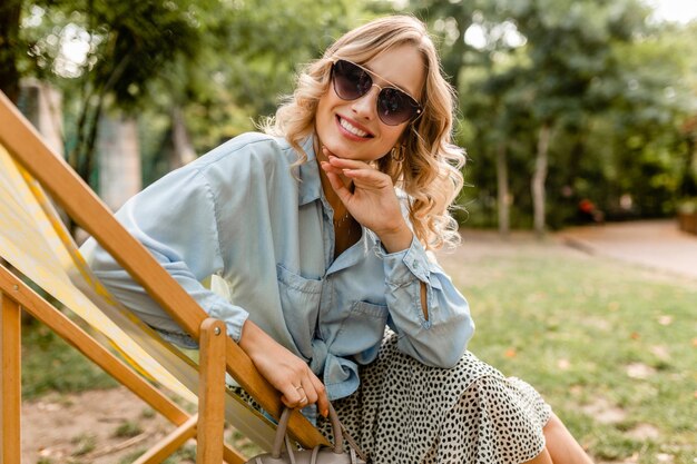 Aantrekkelijke blonde glimlachende vrouwenzitting in ligstoel in de zomeruitrusting