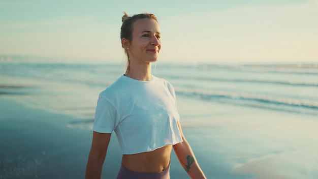 Gratis foto aantrekkelijke blonde vrouw die er gelukkig uitziet terwijl ze frisse lucht inademt tijdens een wandeling langs de zee na yogabeoefening gelukkig meisje dat van de ochtend geniet op het strand