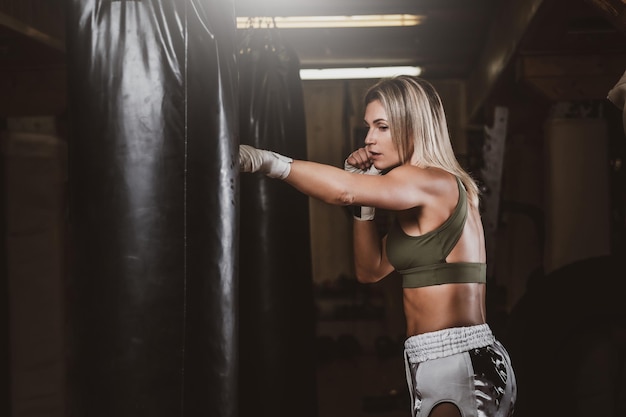 Aantrekkelijke blonde vrouw heeft een bokstraining met bokszak in de kickboksstudio.