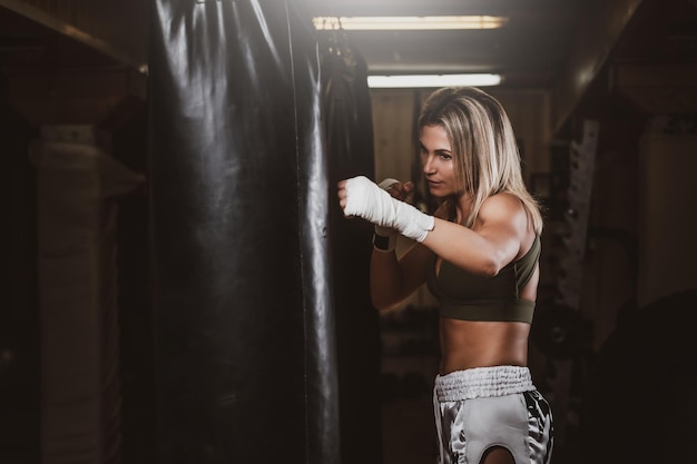 Aantrekkelijke blonde vrouw heeft een bokstraining met bokszak in de kickboksstudio.