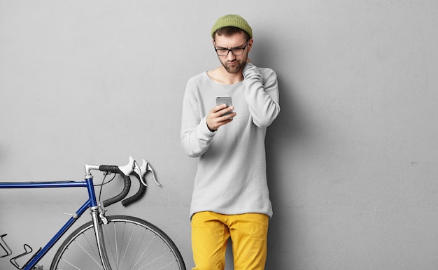 Aantrekkelijke brunette jonge man met baard verward of verbaasd uitdrukking op zijn gezicht terwijl het ontvangen van dringende bericht op e-mail van zijn baas, met behulp van 3g-internetverbinding op de mobiele telefoon