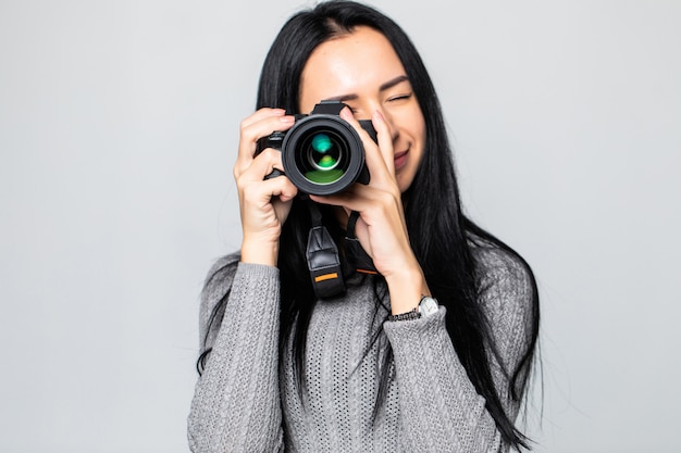 Aantrekkelijke brunette richt haar camera. het samenstellen van een foto in de studio, geïsoleerd op grijze muur