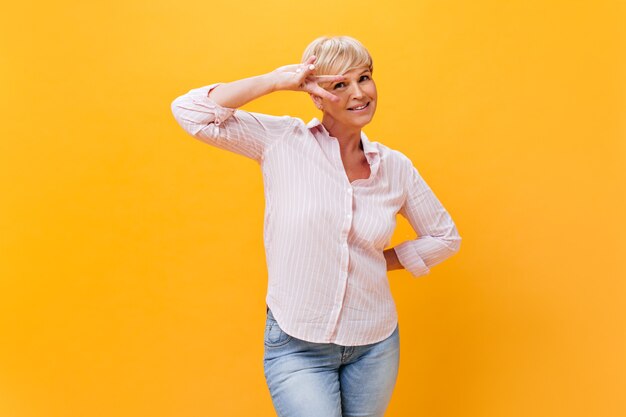 Aantrekkelijke dame in denim broek en roze shirt toont vredesteken