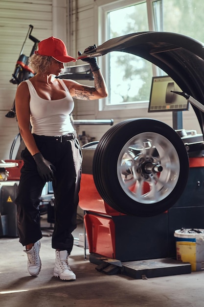 Aantrekkelijke dappere vrouw poseert voor fotograaf in autowerkplaats met een deel van de auto.