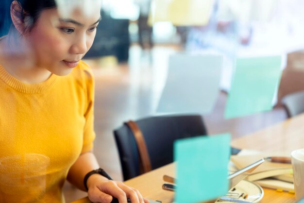 Aantrekkelijke freelance aziatische vrouwelijke creatieve persoon draagt een casual gele doek die met een laptop werkt in een gedeelde ruimte coworking space nieuwe levensstijl met doordachte en frisheid emotie onscherpte kantoorachtergrond