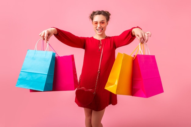 Aantrekkelijke gelukkig grappige emotie stijlvolle vrouw shopaholic in rode trendy jurk met kleurrijke boodschappentassen op roze muur geïsoleerd, verkoop opgewonden, lente zomer modetrend