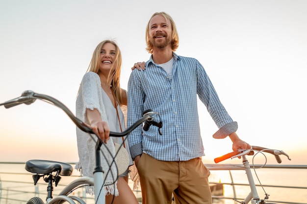 Aantrekkelijke gelukkige paar vrienden reizen in de zomer op fietsen, man en vrouw met blond haar boho hipster stijl mode samen plezier, wandelen aan zee in resort stad