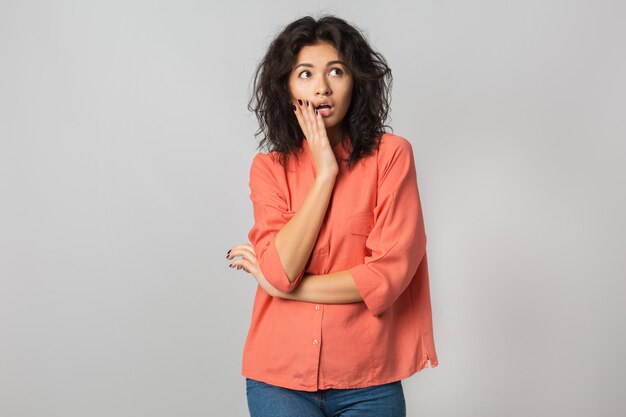 Aantrekkelijke geschokte vrouw die opzij kijkt, verbaasd gezicht, grappige emotie, latijn, oranje blouse, stijlvol, geïsoleerd, jong en natuurlijk