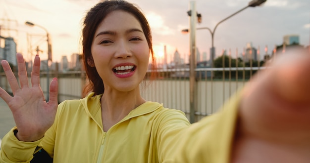 Aantrekkelijke jonge Aziatische atleet influencer dame video vlog live streaming opnemen op telefoon upload in sociale media tijdens oefeningen in stedelijke stad. Sportwoman het dragen van sportkleding op straat in de ochtend.