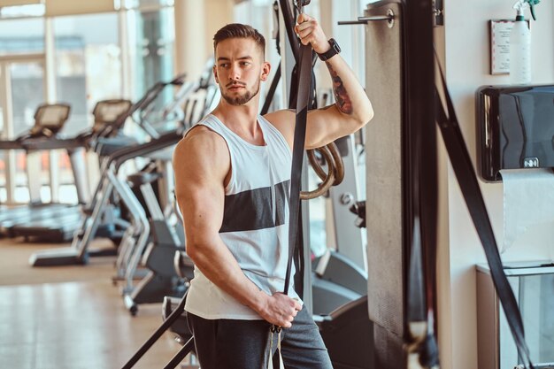 Aantrekkelijke jonge bodybuilder poseert naast trainingsapparatuur op zonnige sportschool.