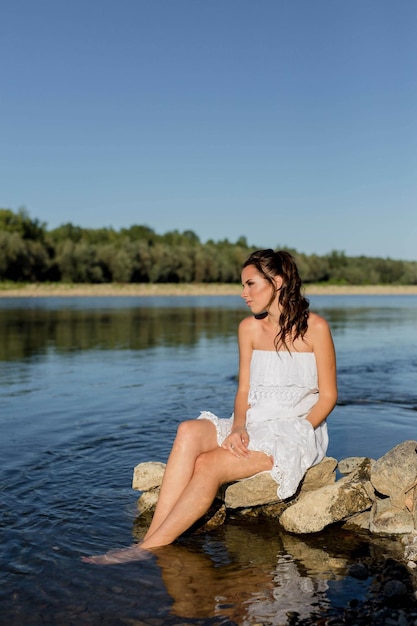 Aantrekkelijke jonge Bosnische vrouw die bij de rivier zit met schattige zomerkleding