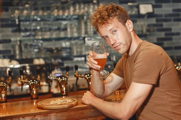 Aantrekkelijke jonge man achter de bar. Man in een bruin T-shirt houdt een glas in zijn handen.