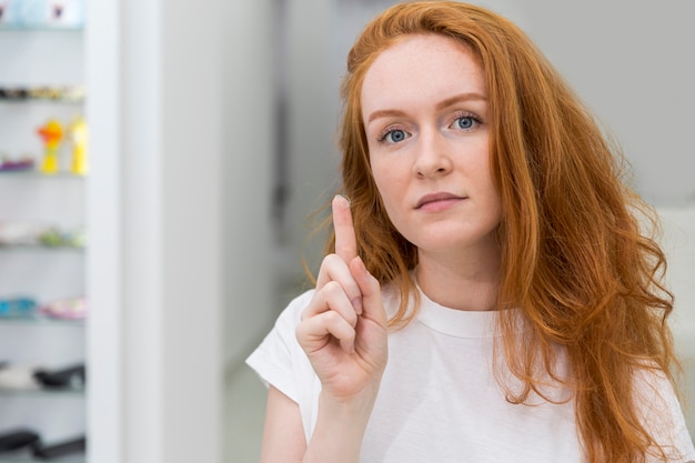 Aantrekkelijke jonge moderne vrouw die contactlens toont en camera bekijkt