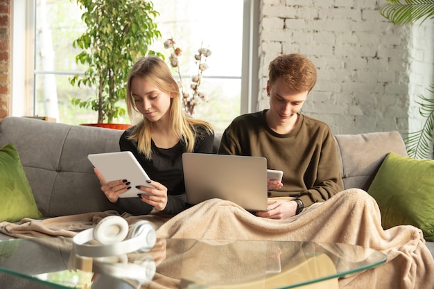 Aantrekkelijke jonge paar apparaten samen gebruiken, tablet, laptop, smartphone, communicatie, gadgets concept. Technologieën die mensen verbinden in zelfisolatie. Levensstijl thuis.