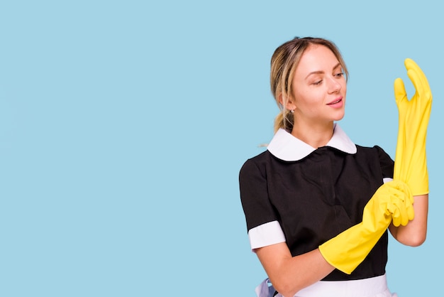Aantrekkelijke jonge vrouw die gele handschoen draagt tegen blauwe achtergrond