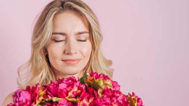 Aantrekkelijke jonge vrouw die het bloemboeket ruikt tegen roze achtergrond