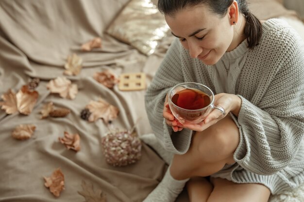 Aantrekkelijke jonge vrouw drinkt thee zittend in bed tussen de herfstbladeren