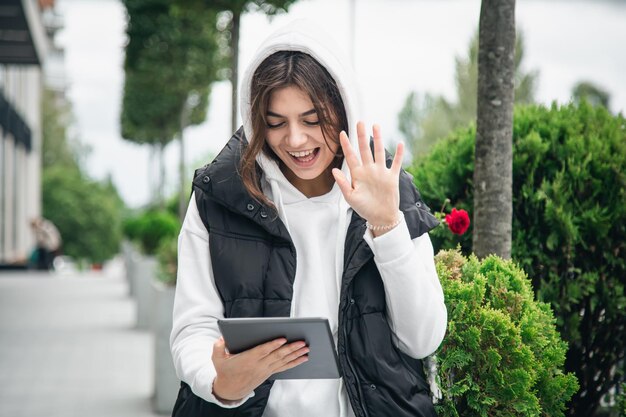 Aantrekkelijke jonge vrouw gebruikt een tablet en communiceert buiten via videogesprek