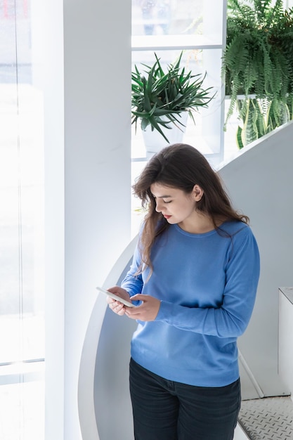 Aantrekkelijke jonge vrouw in een blauwe trui gebruikt de telefoon