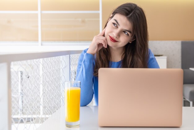 Aantrekkelijke jonge vrouw in een blauwe trui werkt op een laptop in een café
