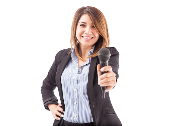 Aantrekkelijke jonge vrouw in een pak die een microfoon overhandigt om te praten, op een witte achtergrond