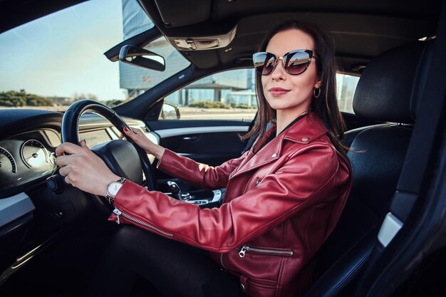 Aantrekkelijke jonge vrouw in rode jas en zonnebril in haar auto rijden.