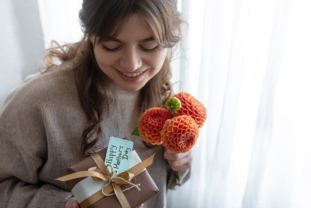 Aantrekkelijke jonge vrouw met een moederdagcadeau en een boeket chrysantenbloemen in haar handen.