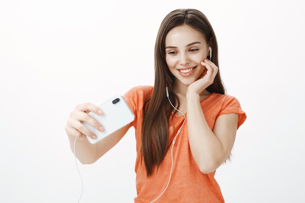 Aantrekkelijke jonge vrouw muziek in hoofdtelefoons luisteren en selfie op mobiele telefoon te nemen