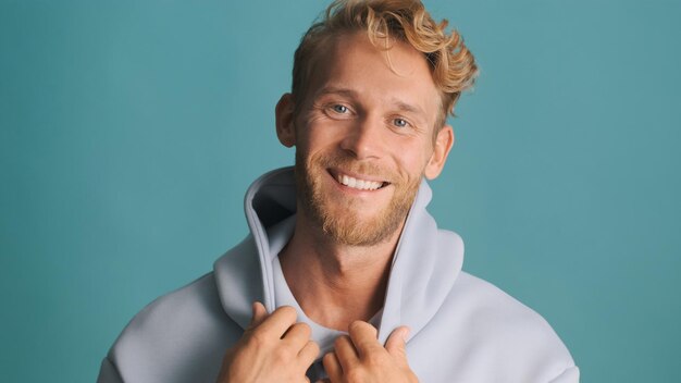 Aantrekkelijke lachende blonde bebaarde man in hoodie vreugdevol tijd doorbrengen met vrienden geïsoleerd op blauwe achtergrond Goed humeur